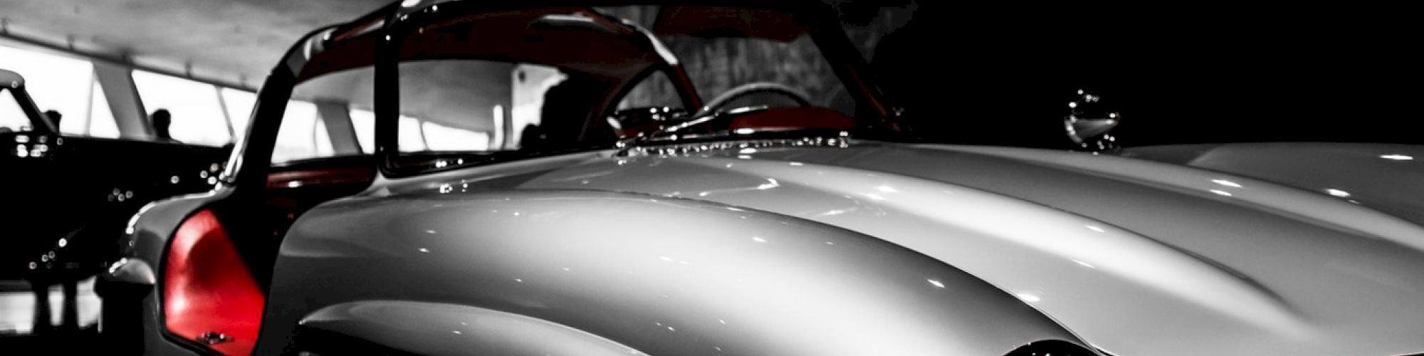 A classic gullwing car with its doors open, showcasing a sleek silver body and red interior, displayed in a dimly lit setting.