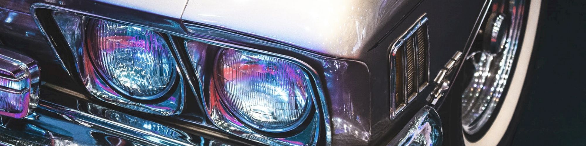 A close-up shot of the front corner of a classic car, showcasing its headlights and chrome details with the name 