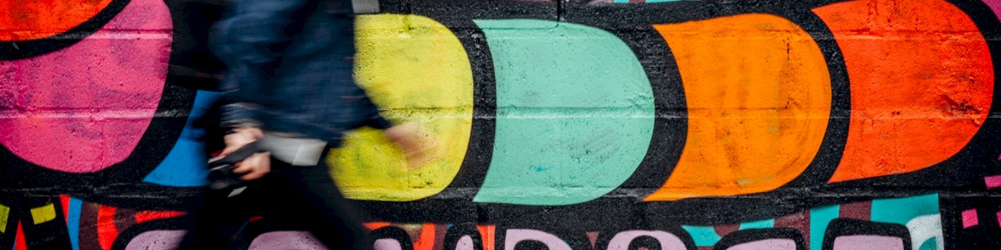 A person walks by a colorful graffiti mural featuring abstract shapes, hearts, stars, and the word 