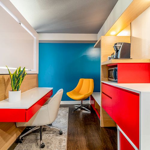 A modern office space with colorful furniture, including a yellow chair, red cabinets, white desk, and a plant, against a blue accent wall.