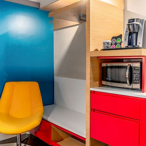 A bright kitchen nook with a yellow chair, blue wall, and red cabinets. Includes a microwave, coffee maker, and K-cups.