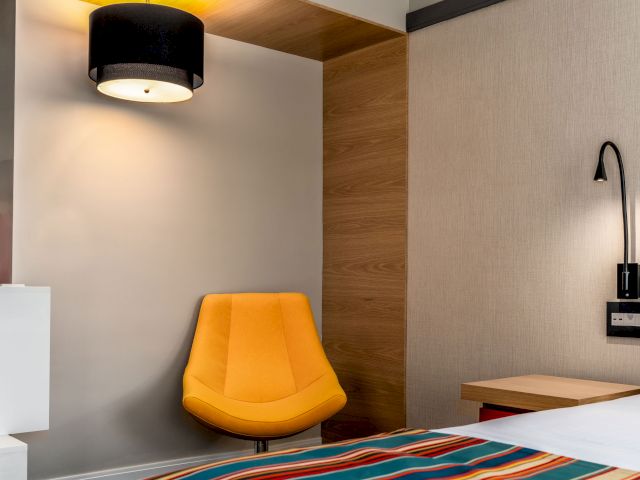 A hotel room with a bed, chair, and lamps