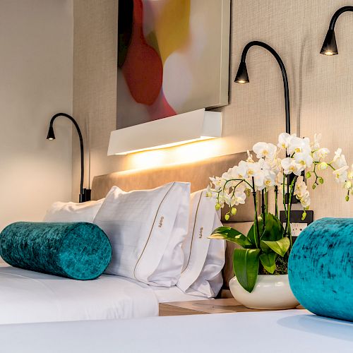 A cozy bedroom setup with two beds, turquoise bolster pillows, flowers on a nightstand, modern reading lamps, and abstract wall art ends the sentence.