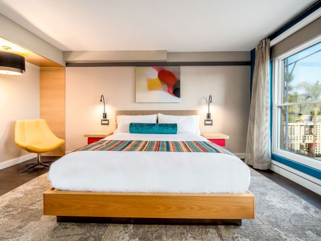 A wide view of a hotel room with a large bed, nightstands, a chair, and a window.