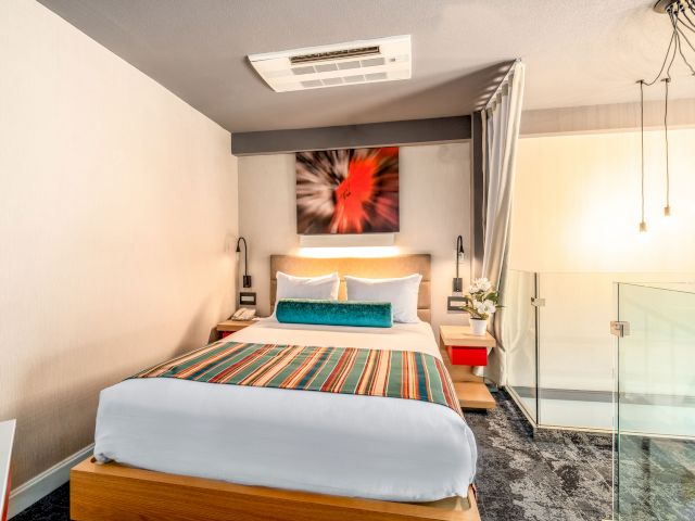 A hotel room with a bed, nightstands, and artwork on the wall.