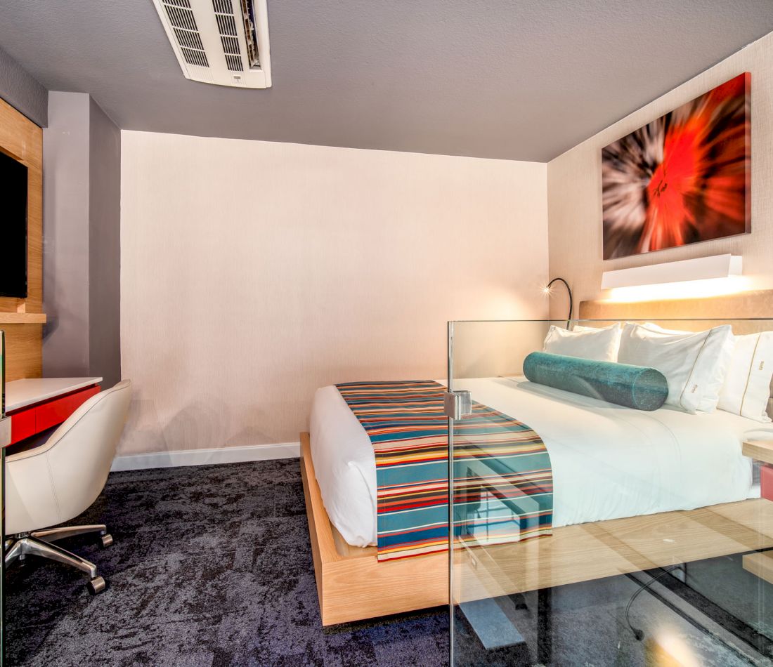 A hotel room with a bed, desk, chair, and television.