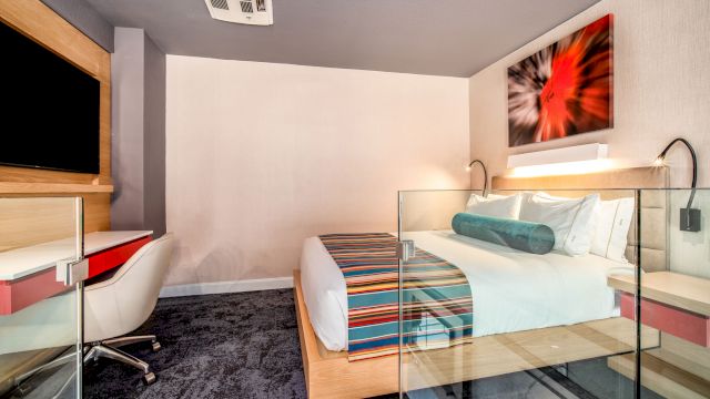 A wide view of a hotel room with a bed, desk, TV, and artwork.