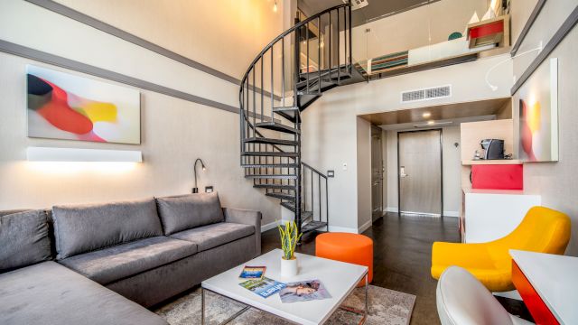 A modern living room with a spiral staircase, gray sectional sofa, white coffee table, and colorful armchairs.