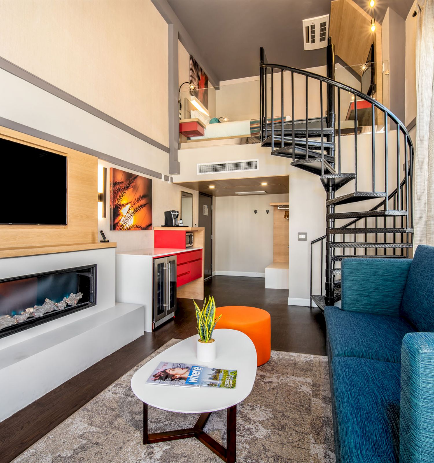 A modern living area features a spiral staircase, a blue sofa, a wall-mounted TV, a fireplace, a small table, and vibrant orange accents, ending the sentence.