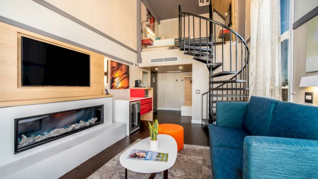 A modern living room with a TV, fireplace, blue sofa, and spiral staircase.