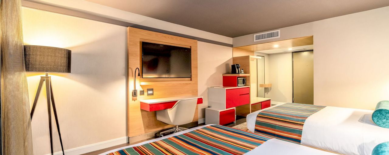 A hotel room with a bed, desk, TV, and kitchenette.