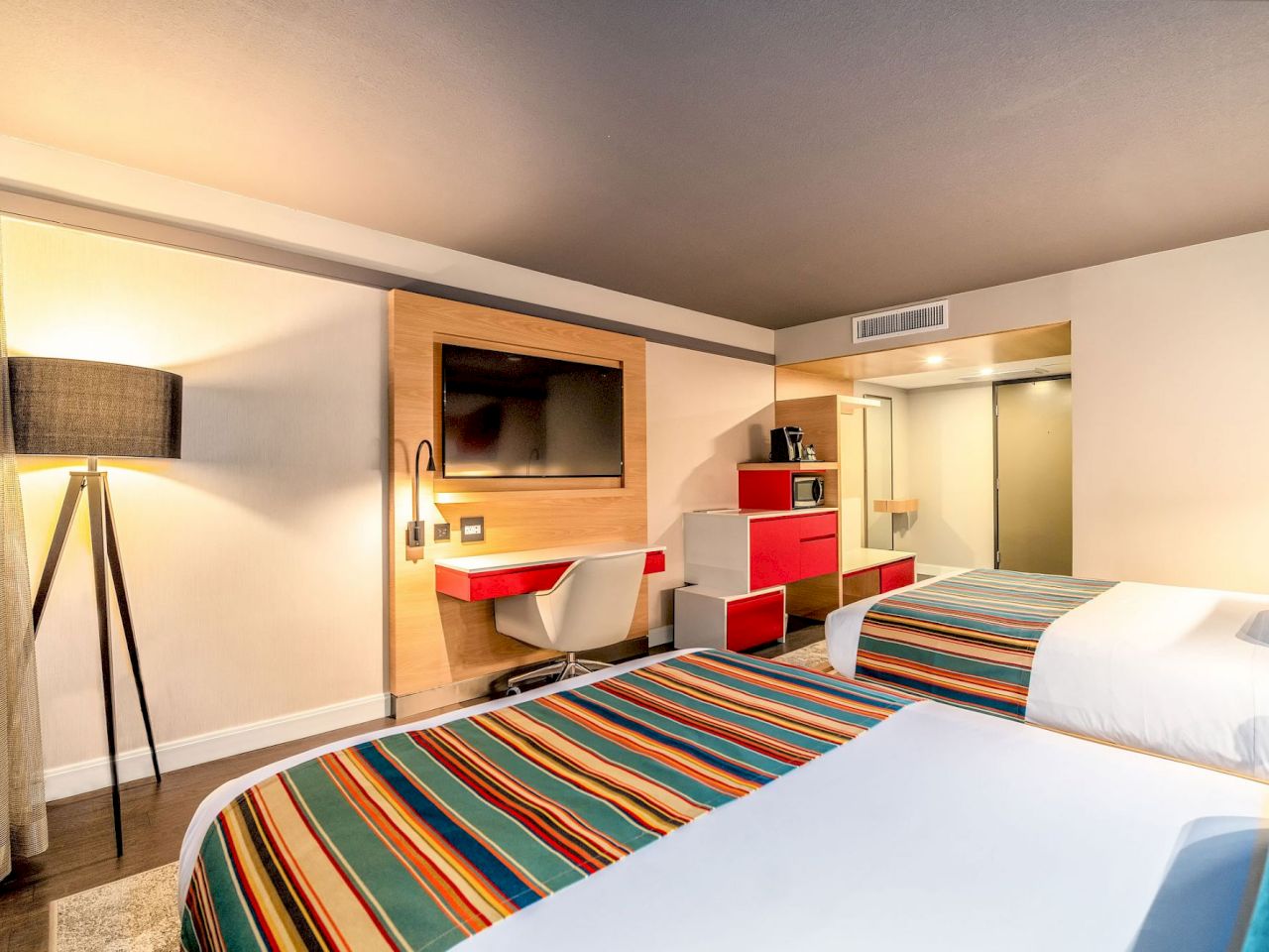 A hotel room with two beds, a TV, desk, and mirror.