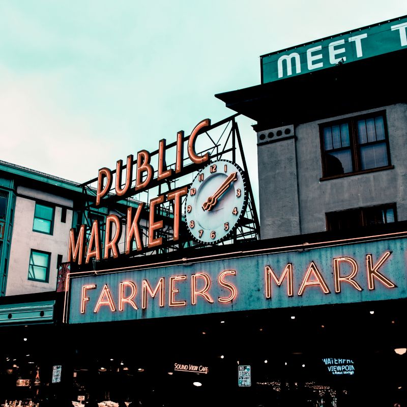 A neon sign reading "Public Market" and "Farmers Market" with a large clock is prominently displayed on a building in this image.