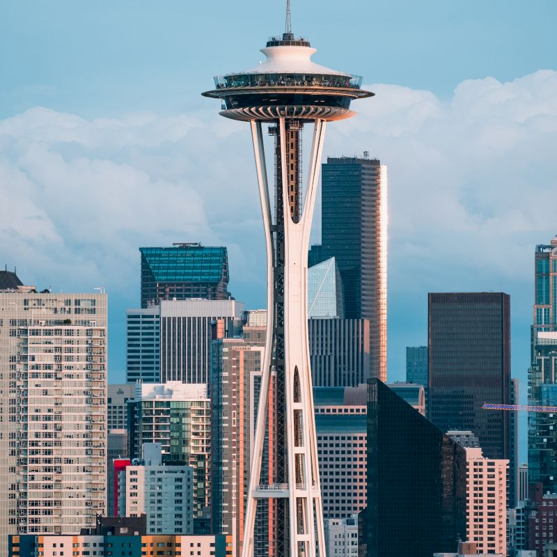 The image features the Space Needle, a famous observation tower, with the Seattle skyline in the background under a blue sky with scattered clouds.