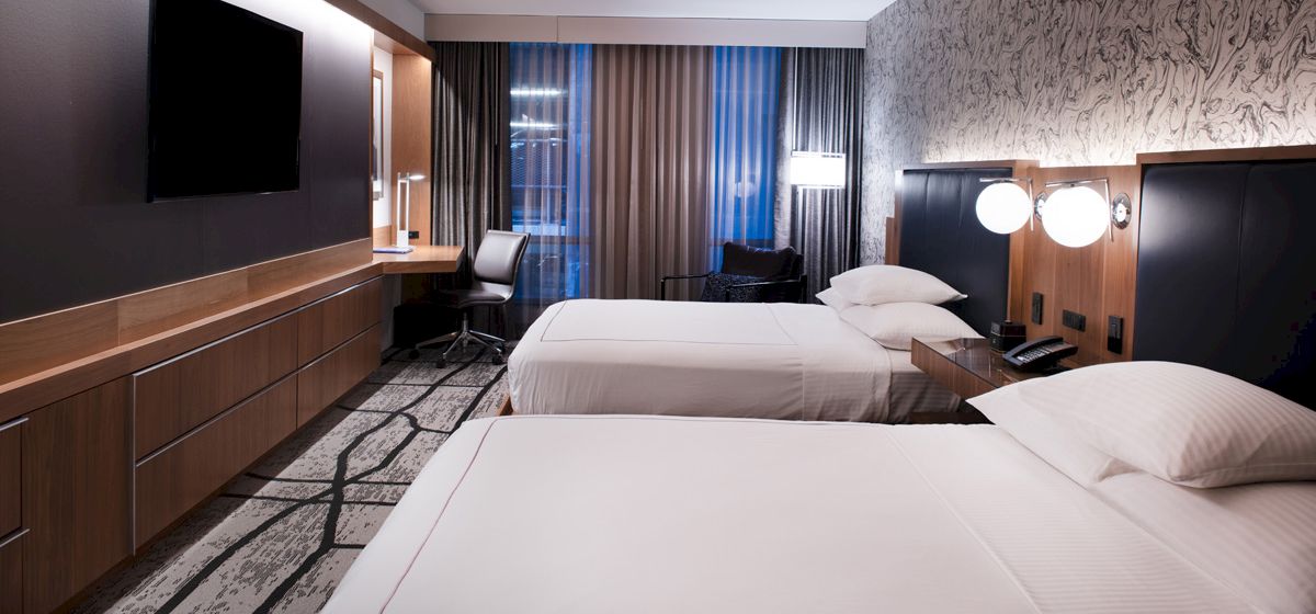 A hotel room with two double beds, a desk, TV, and lamps.
