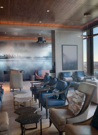This image shows a lounge area with modern chairs and tables, large windows with cityscape views, and a mural on the back wall.