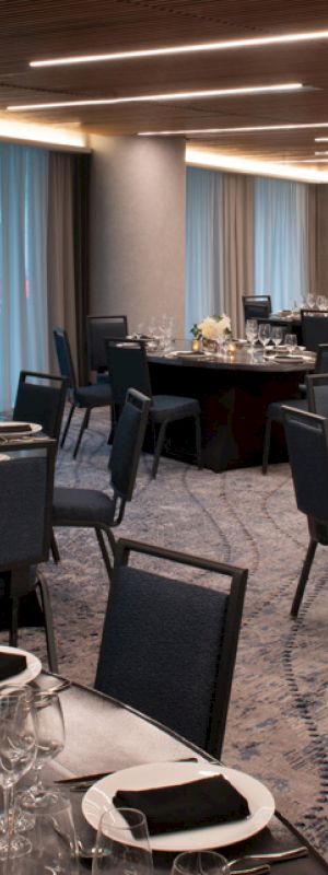 A banquet hall set up with round tables covered in black tablecloths, elegant place settings, and black napkins, ready for an event or dinner.