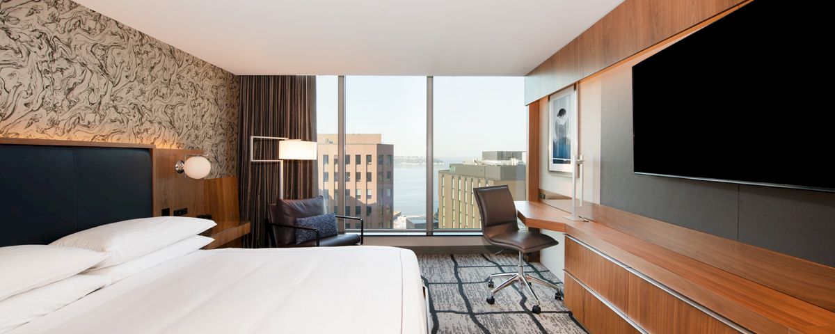 A hotel room with a bed, TV, desk, and window