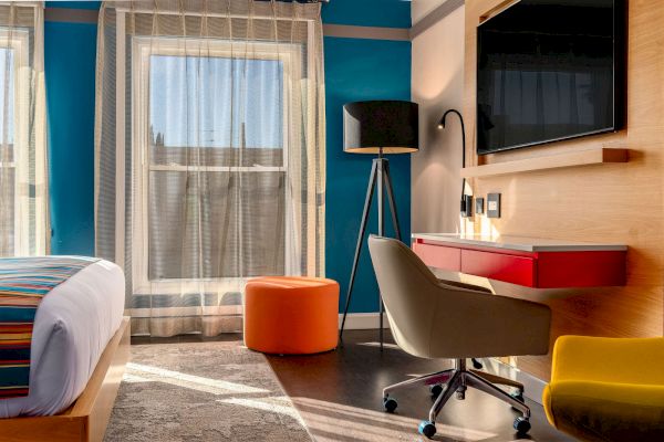 A hotel room with a bed, desk, chair, and TV