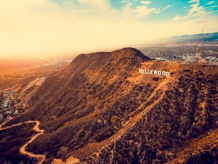 Aerial view of the iconic Hollywood sign located on a hillside with a view of the city and mountains in the background during sunset.