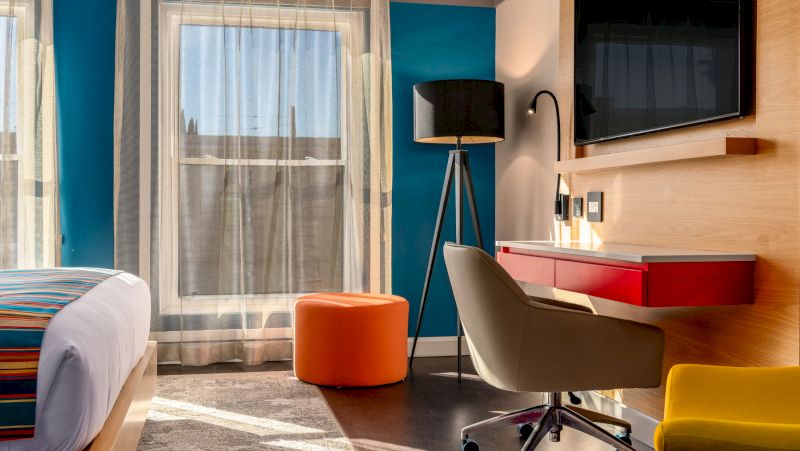 A hotel room with a bed, desk, chair, and TV.