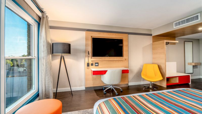 A hotel room with a desk, TV, bed, and chair.