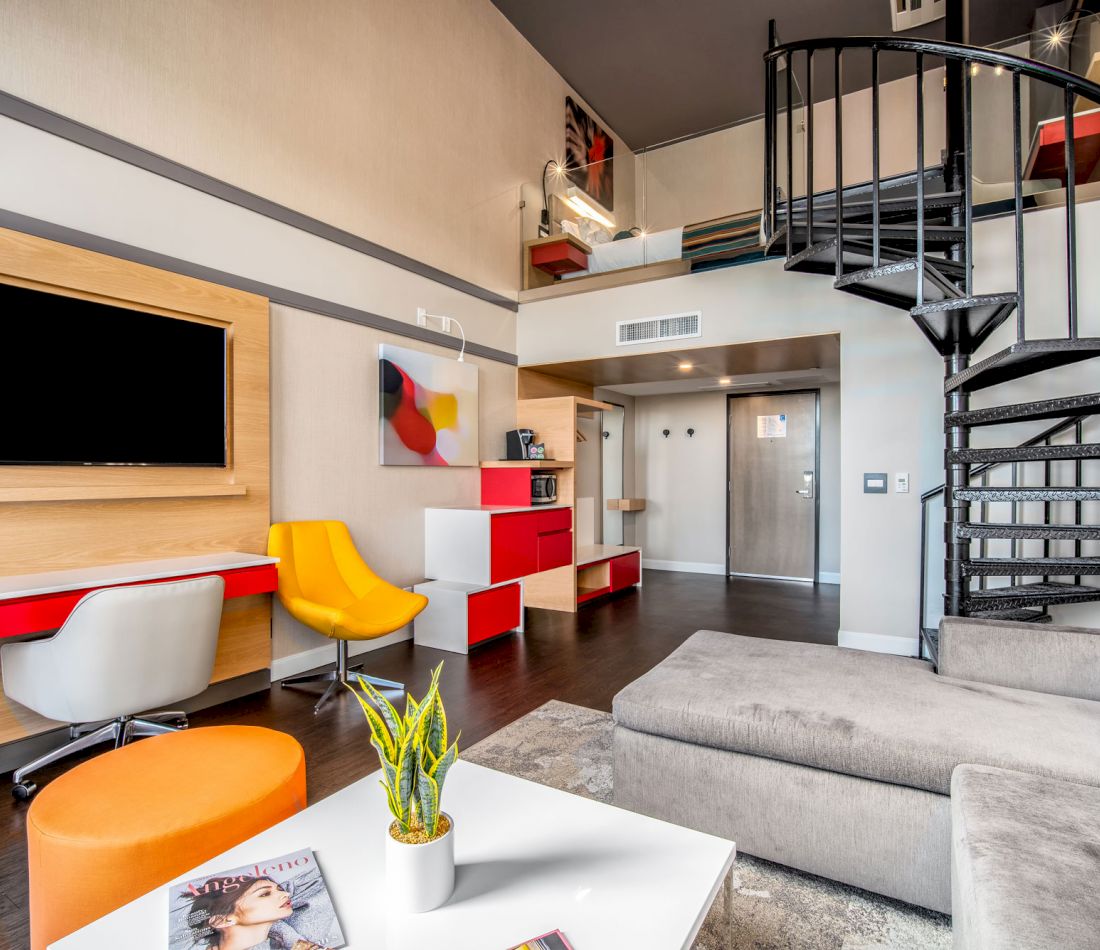 A modern lobby with a sofa, coffee table, TV, desk, chair, and staircase.