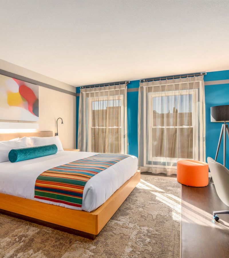 A wide view of a hotel room with a bed, desk, chair, and window